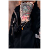 Goldenes Armband mit Smiley-Anhänger an tätowiertem Handgelenk