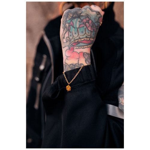 Goldenes Armband mit Smiley-Anhänger an tätowiertem Handgelenk