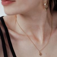Dame mit goldener Little Sunflower Kette, filigran und elegant, auf hellem Hintergrund
