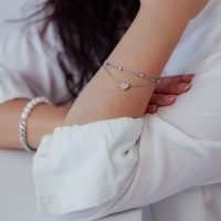 Silbernes zweireihiges Armband mit Herzanhänger am Arm einer Person in weißer Kleidung