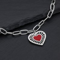 Silberfarbenes Armband aus Chirurgenstahl mit rotem Herzanhänger auf dunklem Hintergrund