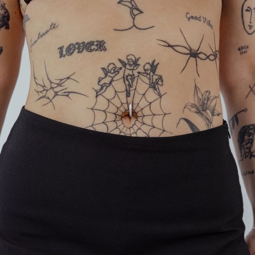 Bauchnabel Clicker aus schwarzem Titan mit klarem Kristall auf Haut mit Tattoos