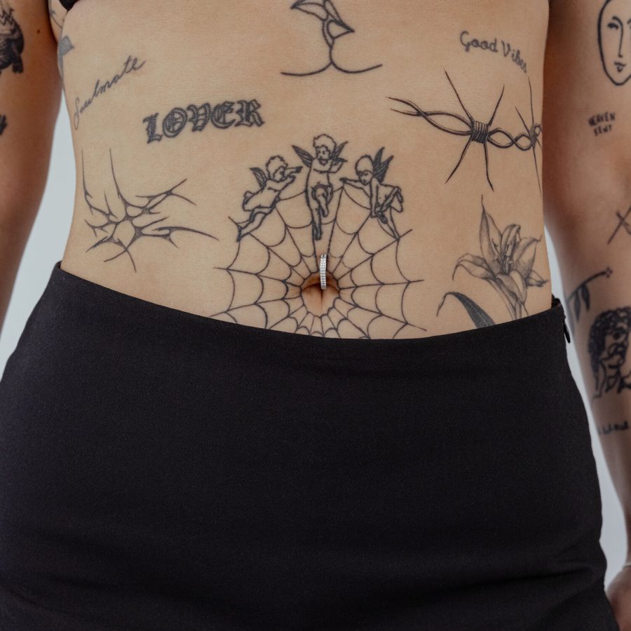 Bauchnabel Clicker aus schwarzem Titan mit klarem Kristall auf Haut mit Tattoos