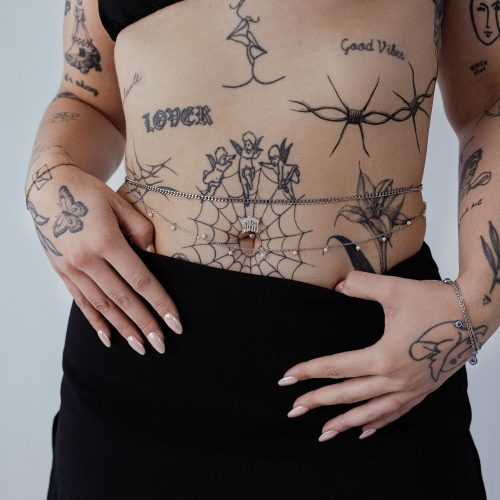 Frau mit doppelter Bauchketten aus Chirurgenstahl, Tattoos sichtbar, schwarzer Rock