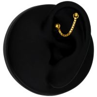 Goldene Piercingkette aus 585er Gold an einem schwarzen Ohr auf schwarzem Hintergrund