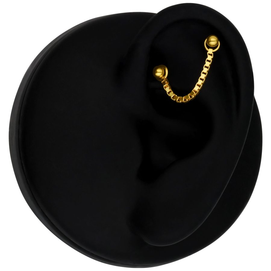 Goldene Piercingkette aus 585er Gold an einem schwarzen Ohr auf schwarzem Hintergrund