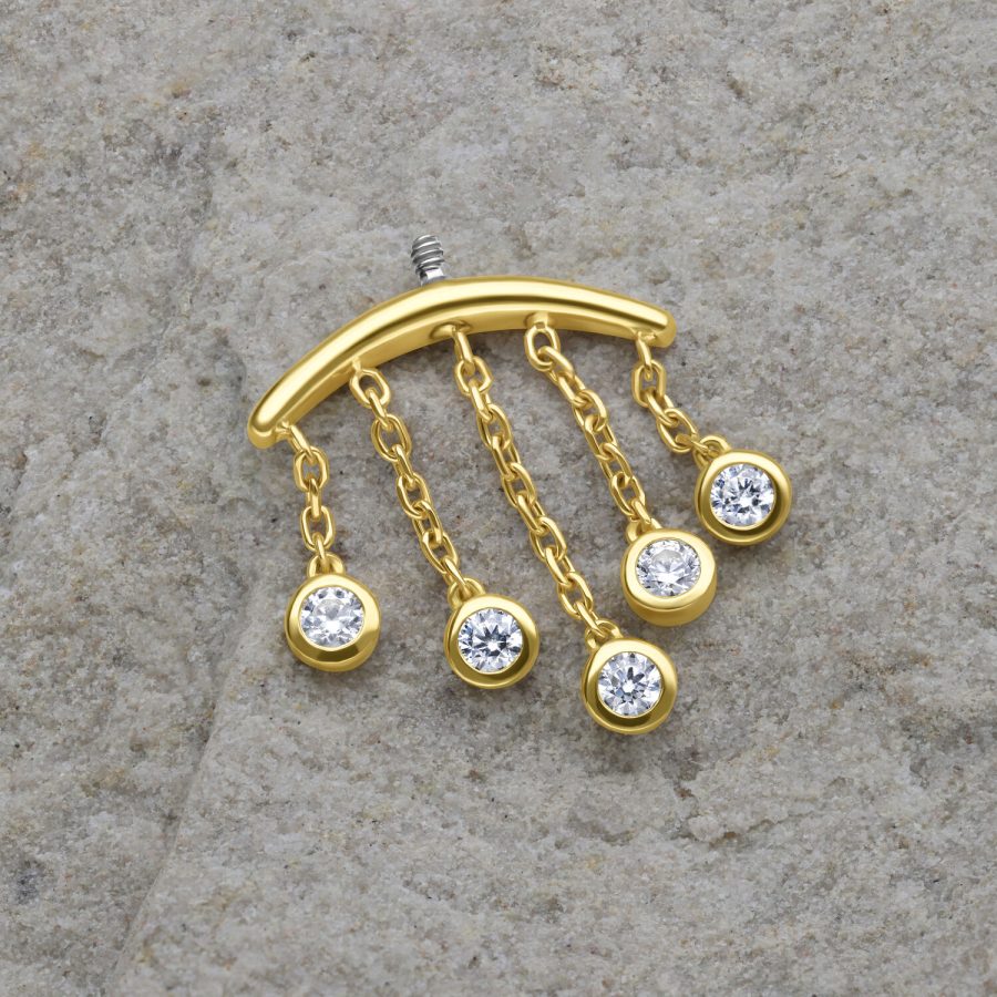 Goldener Piercing-Aufsatz mit fünf klaren Kristalltropfen auf grauem Hintergrund