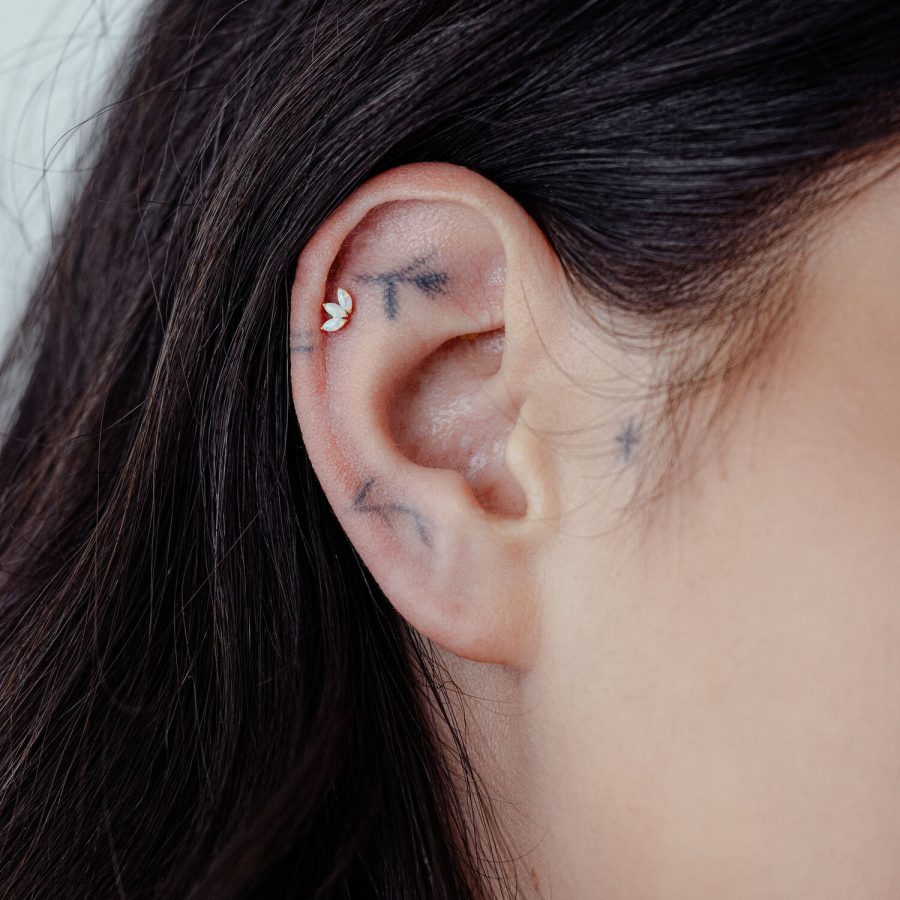 Nahaufnahme eines Ohrpiercings mit 14K Gold Lotus und synthetischem Opal an einem Ohr