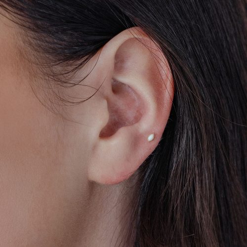Ovaler Goldaufsatz mit synthetischem Opal im Ohr auf hellem Hintergrund