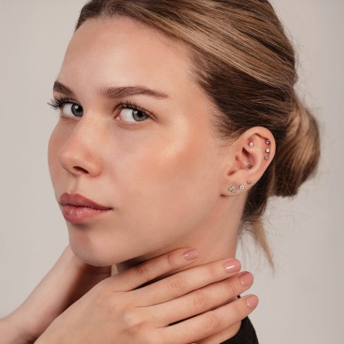 Frau mit Trinity Piercing-Aufsatz im Ohr, verschiedene Kristallfarben