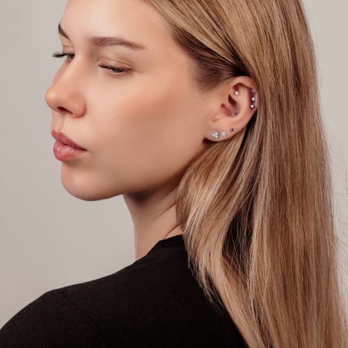 Frau mit mehreren Piercings und Kristallkugel-Ohrring auf hellem Hintergrund
