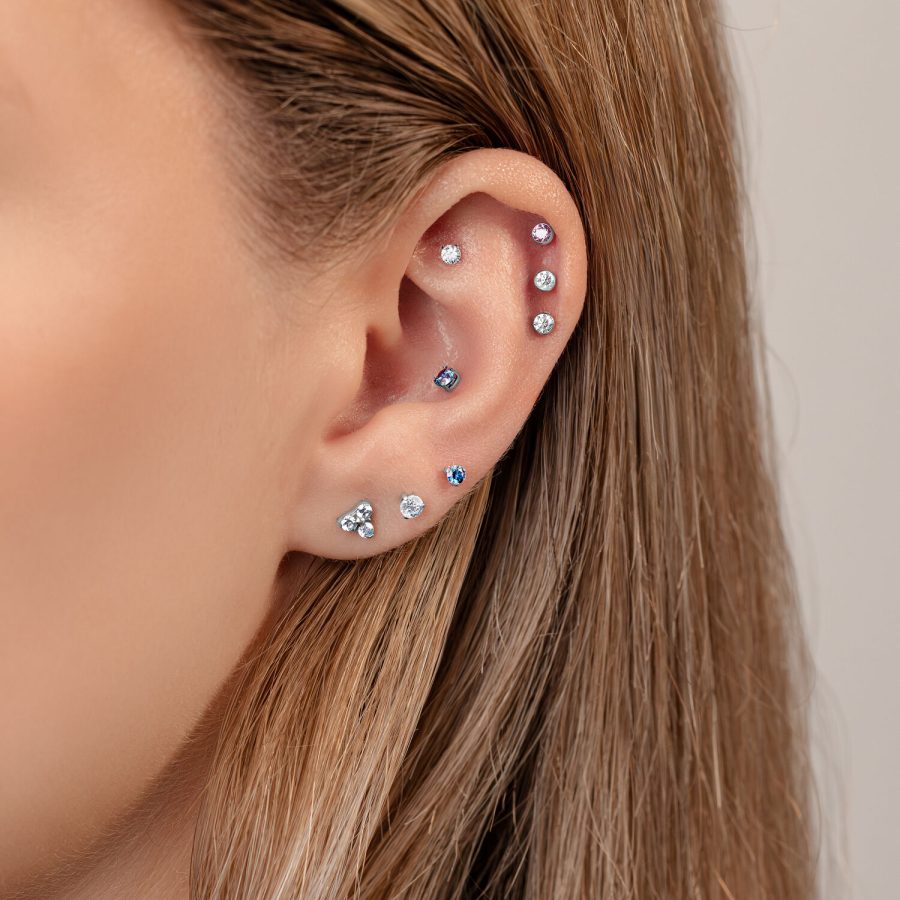 Nahaufnahme eines Ohrs mit mehreren Piercings, darunter ein 3-Prong Aufsatz in Kristallfarben