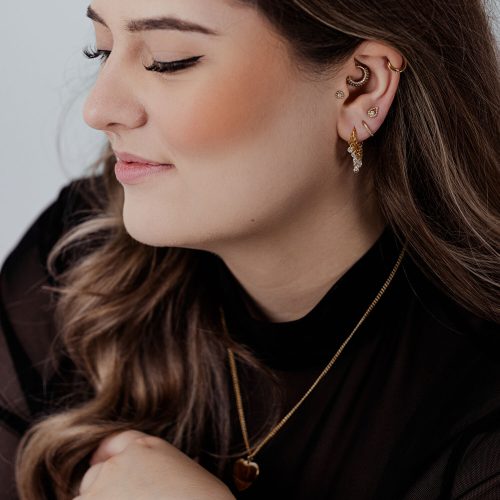 Frau mit goldenen Piercingringen und Kristallen im Ohr auf hellem Hintergrund
