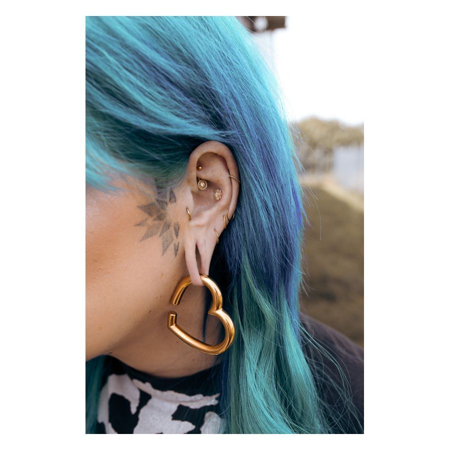 Goldenes Bananabell Piercing in Ohr mit blauem Haar und Herz-Ohrring.