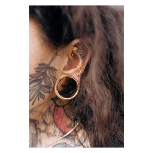 Roségoldenes Bananabell Piercing im Ohr mit Tattoo im Hintergrund