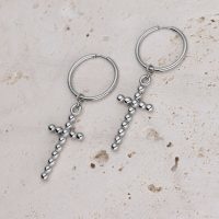 Zwei silberne Creolen mit Kreuzanhängern auf hellem Stein