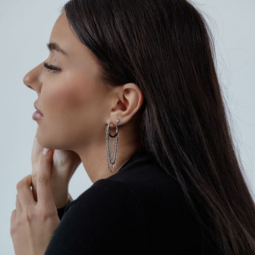 Frau mit schwarzen Haaren trägt silberne Multilayer Chain Hoops auf hellem Hintergrund