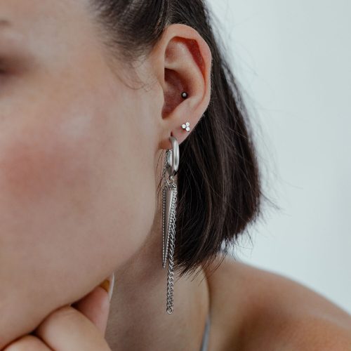 Silberne Triangle Ohrstecker am Ohr einer Frau mit kurzen Haaren vor hellem Hintergrund