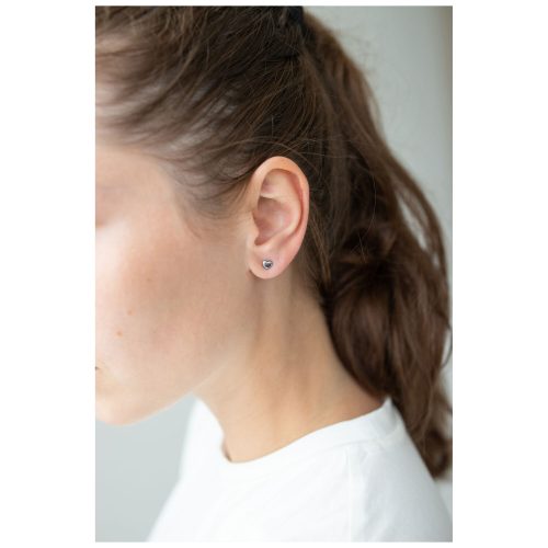 Silberne Herz Ohrstecker am Ohr einer Frau mit braunen Haaren, weißer Hintergrund