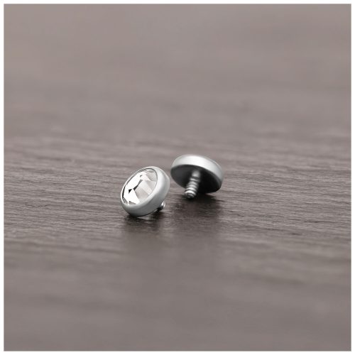 Silberner Piercing-Aufsatz aus Titan mit klarem Kristall auf Holzoberfläche liegend