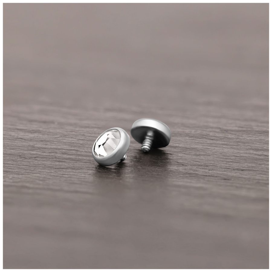 Silberner Piercing-Aufsatz aus Titan mit klarem Kristall auf Holzoberfläche liegend