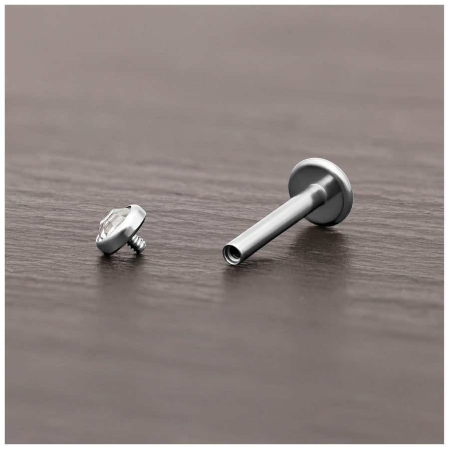 Silberner Titan Piercing-Aufsatz mit klarem Kristall auf dunklem Holz.