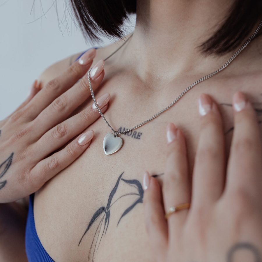 Silberne Kette mit gravierbarem Herzanhänger auf Haut mit Tattoos
