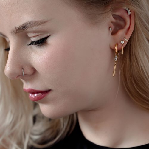 Frau mit mehreren Piercings, darunter ein goldener Kristall-Piercingaufsatz im Ohr.
