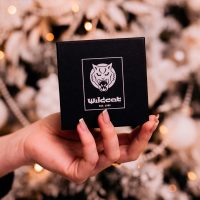 Schwarze Geschenkbox von Wildcat mit Opal Halskette und Silber Creolen, gehalten von einer Hand vor unscharfem Hintergrund