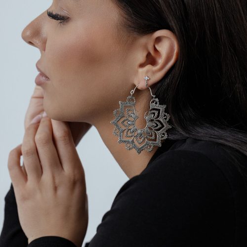 Frau mit eleganten Sunburst Hoops Ohrringen in Silber und Gold vor hellem Hintergrund
