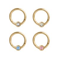 Vier goldene Piercing-Ringe mit klaren, blauen, rosa und schimmernden Kristallen auf weißem Hintergrund