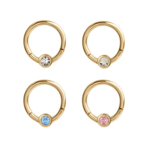 Vier goldene Piercing-Ringe mit klaren, blauen, rosa und schimmernden Kristallen auf weißem Hintergrund