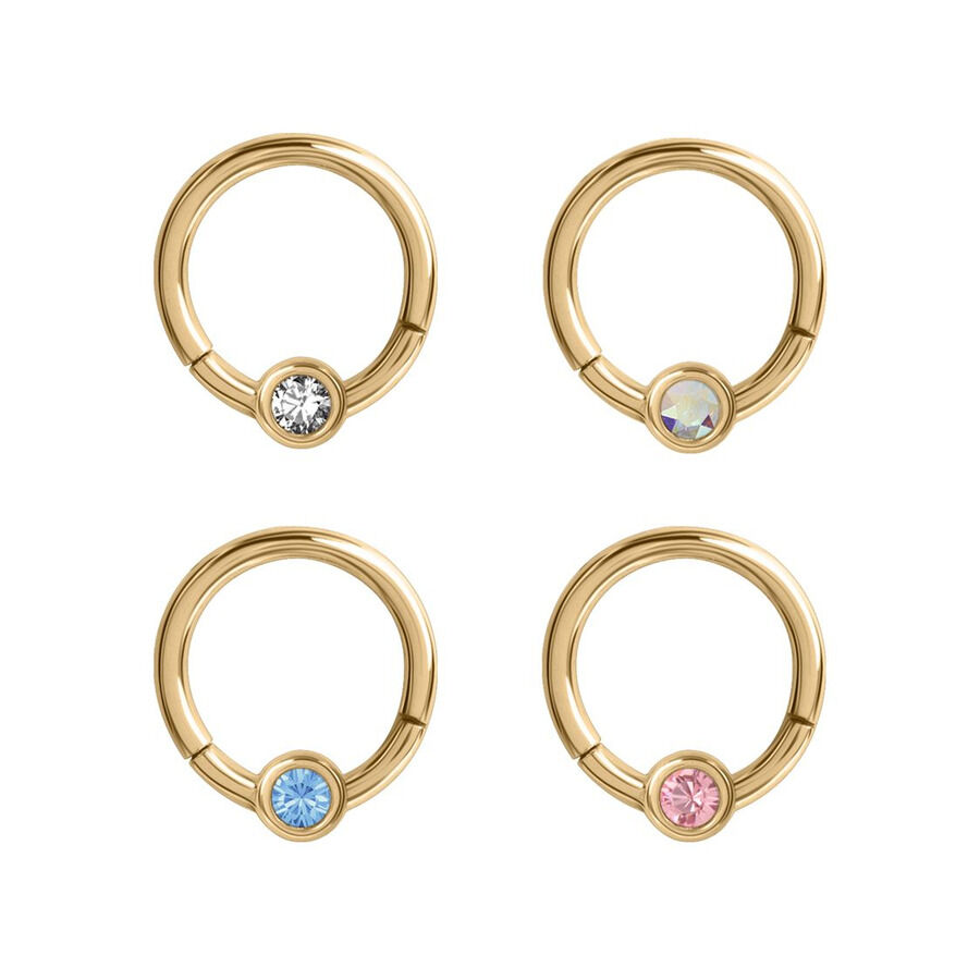 Vier goldene Piercing-Ringe mit klaren, blauen, rosa und schimmernden Kristallen auf weißem Hintergrund