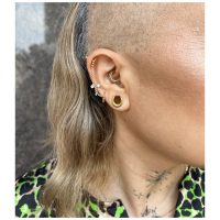 Nahaufnahme eines Ohres mit mehreren goldenen Piercingringen und Kristallen