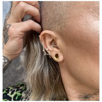 Goldener Piercingring mit kleinen Kristallkugeln an einem Ohr mit mehreren Piercings.
