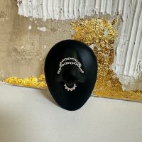 Silberne Piercingkette auf schwarzem Ständer vor gold-weißer Wand