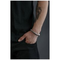 Silberfarbenes Bubble Armband an einem tätowierten Handgelenk vor grauem Hintergrund