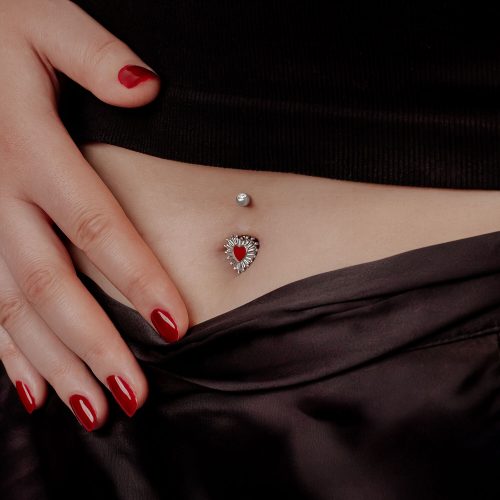 Frau mit rotem Nagellack zeigt Sacred Heart Bananabell im Bauchnabel