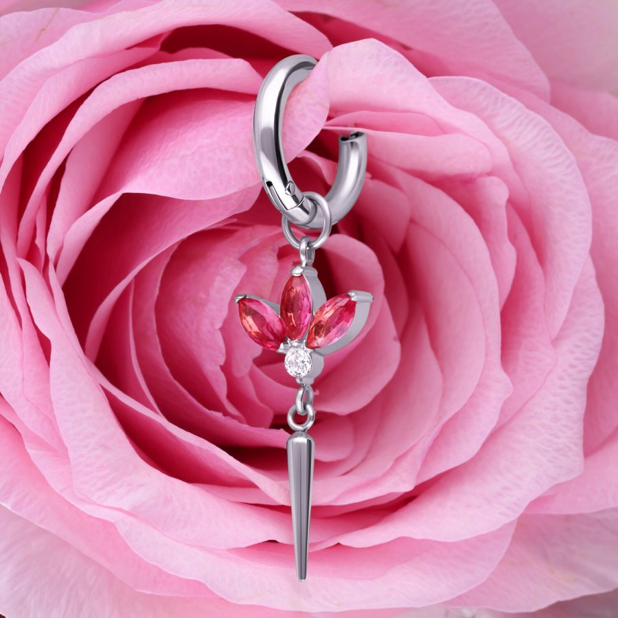 Silberner Ohrring mit roten Kristallen, in Blütenform, vor rosa Rose