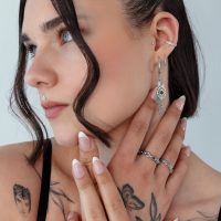 Frau mit silbernen Moos Achat Ohrringen und Tattoos vor hellem Hintergrund