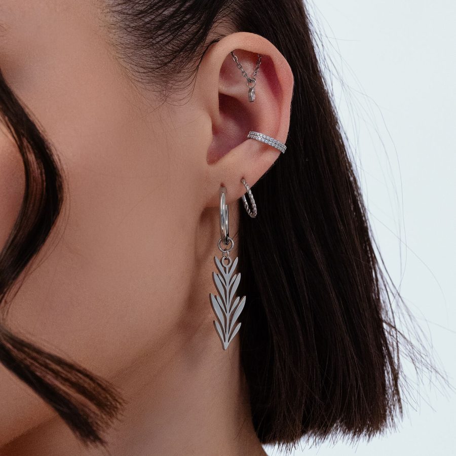Nahaufnahme eines Ohrs mit silbernen Ohrringen im Blattdesign, mehrere Piercings