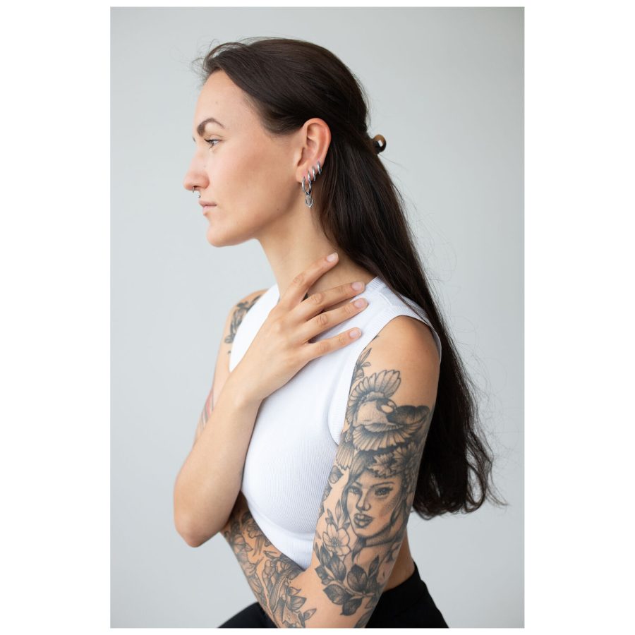 Frau mit langen Haaren und tätowierten Armen, trägt silberne Little Anchor Hoops Ohrringe