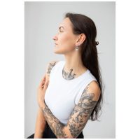 Frau mit langen Haaren trägt stilvolle Little Flower Hoops Ohrringe auf grauem Hintergrund