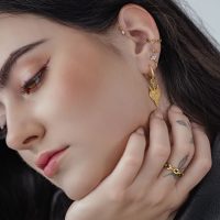 Nahaufnahme von goldenen Herz Creolen am Ohr einer Frau mit dunklen Haaren