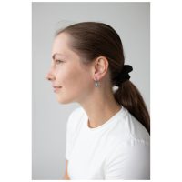 Frau mit braunem Haar trägt schwarze Gummi-Bärchen-Ohrringe, weißes Shirt.