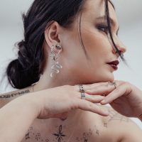 Frau mit silbernen Little Cross Hoops und Schlangenohrring, weißer Hintergrund