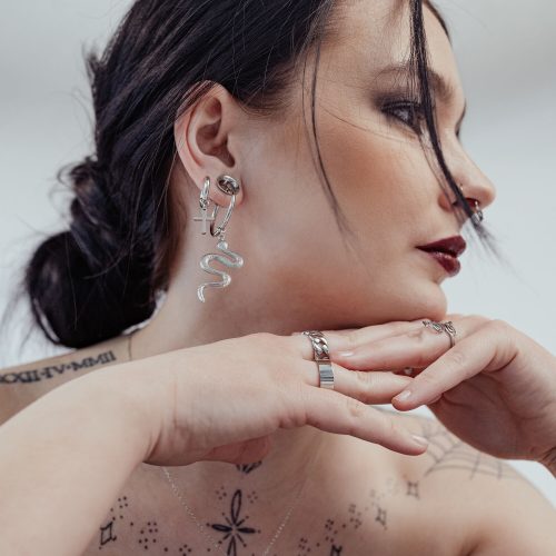 Frau mit silbernen Little Cross Hoops und Schlangenohrring, weißer Hintergrund