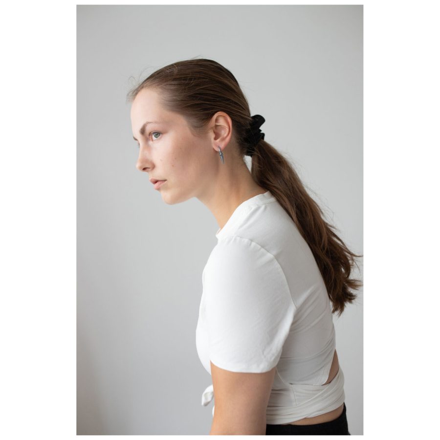 Frau mit langen, glatten Haaren trägt Spike Ohrringe aus schwarzem und silbernem Chirurgenstahl, weißes Oberteil.