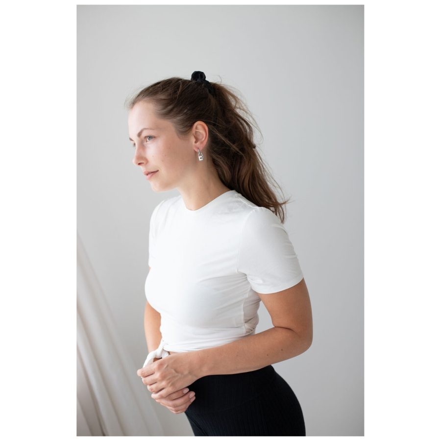 Frau mit weißen T-Shirt und eleganten silbernen Ohrringen vor neutralem Hintergrund