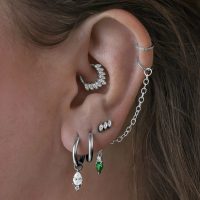 Mehrere Ohrringe im Ohr, darunter schwarze Little Tear Hoops mit grünem Kristall.